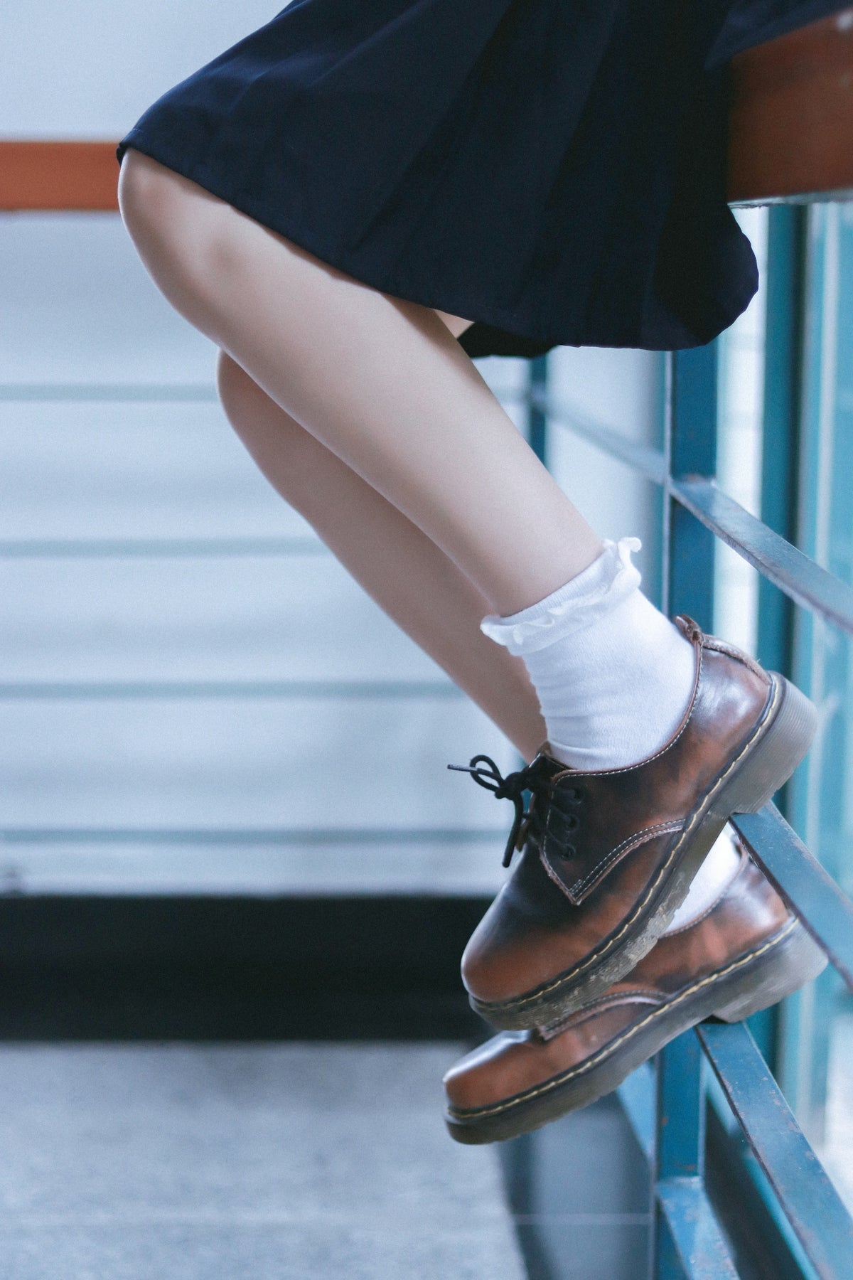 Young person in school uniform and brown shoes sits.