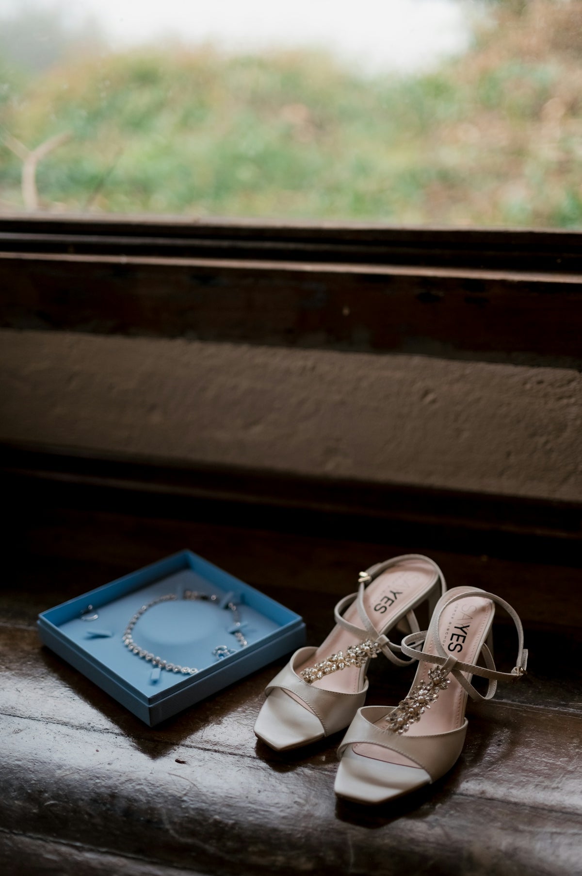 Elegant wedding shoes and necklace on a wooden windowsill.