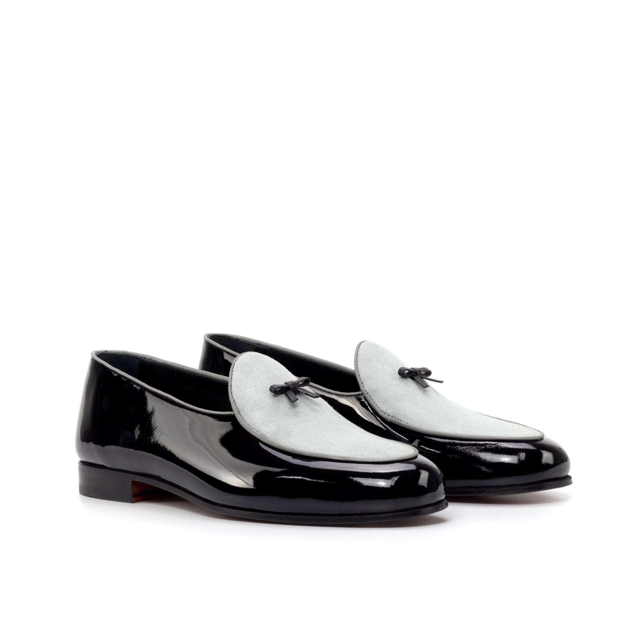 Black patent leather loafers with white accents on a white background