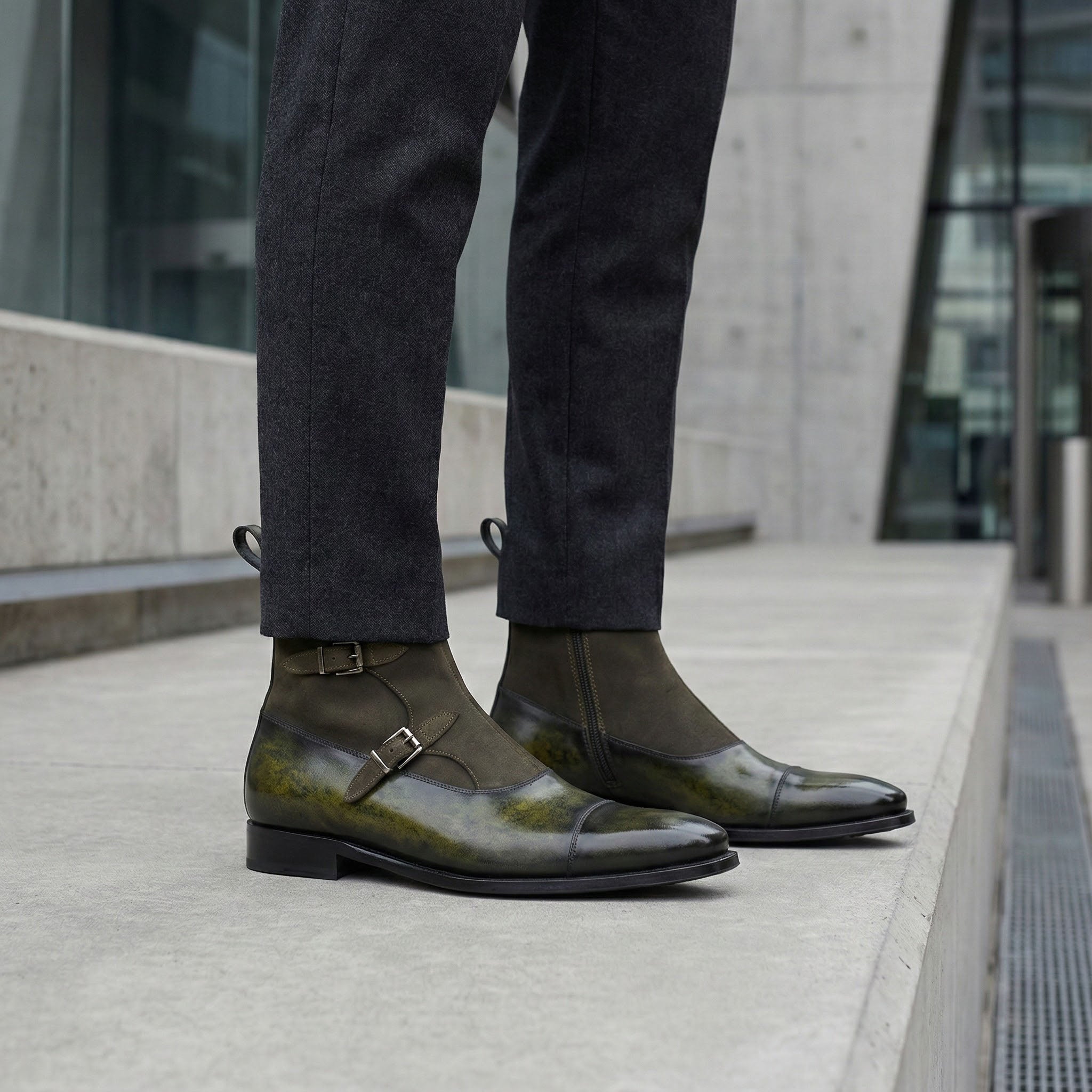 Person wearing dark green leather shoes with a building in the background