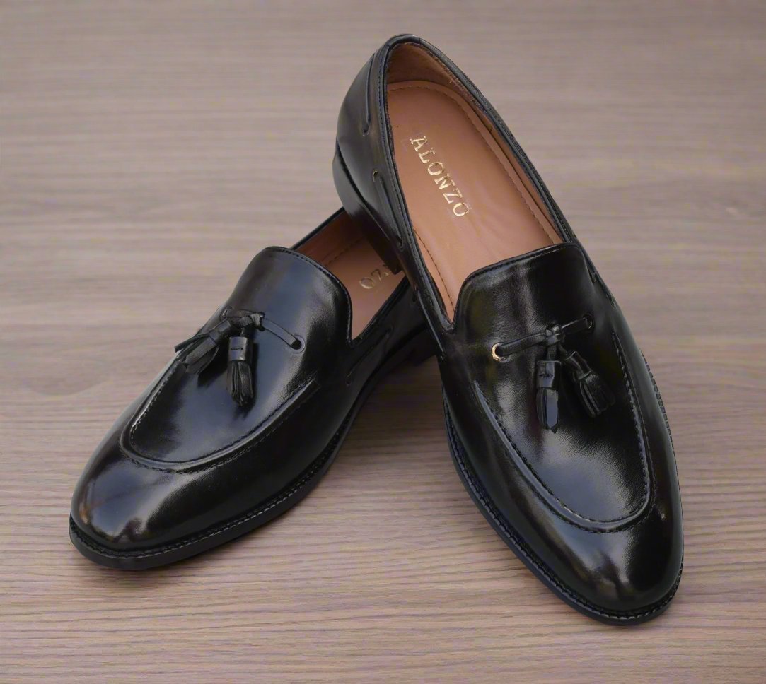 Arconya - A pair of handmade black loafers with a round toe shape and a hand-stitched border on a wooden surface.