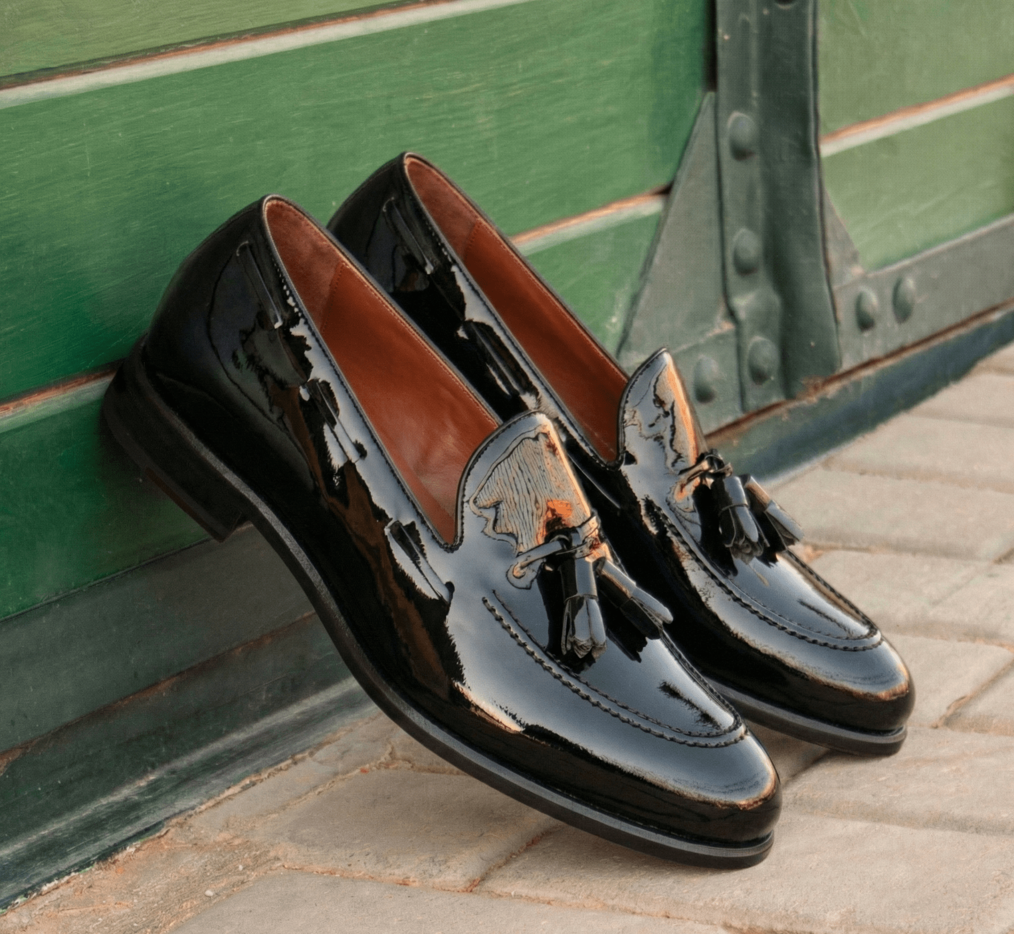Pair of black loafers with brown interior on a stone surface against a green wooden background
