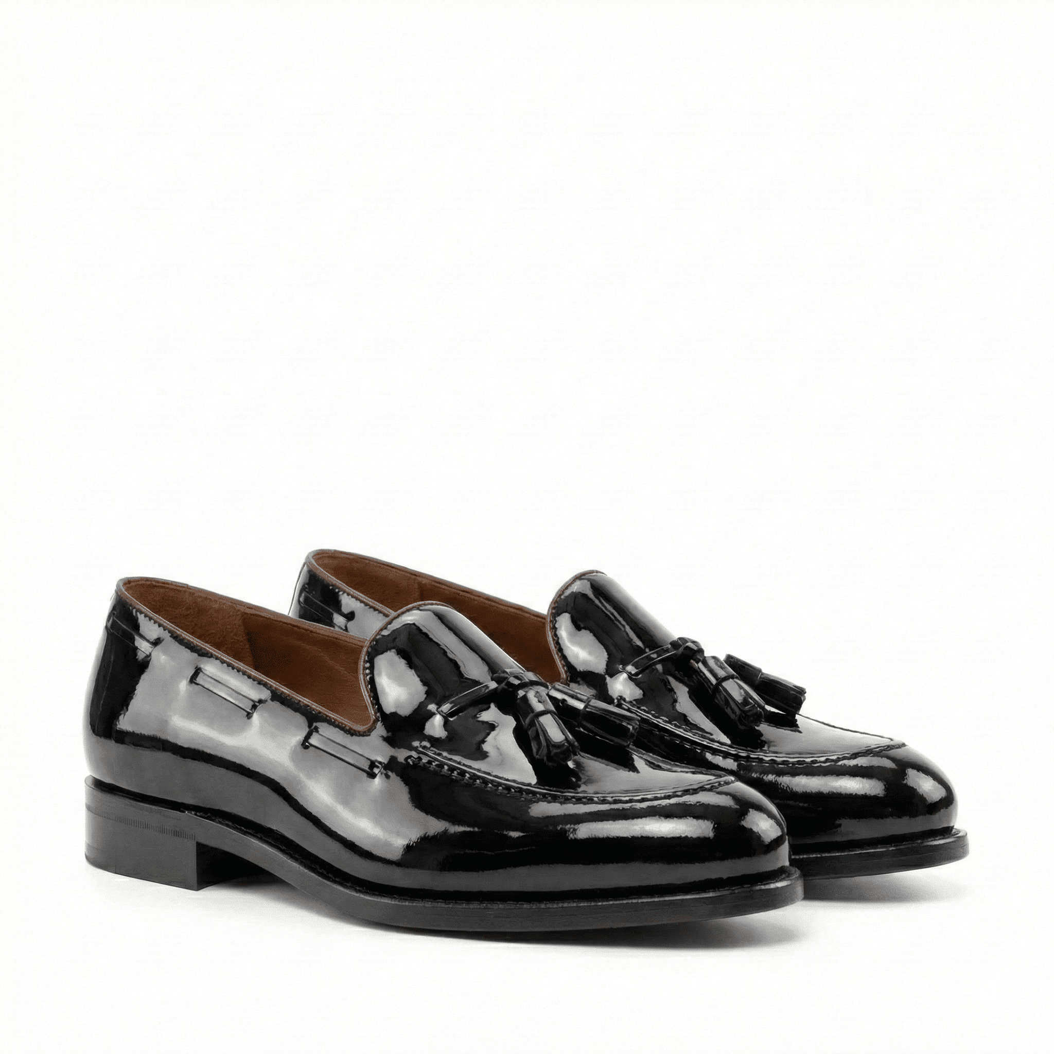 Pair of black patent leather loafers with tassels on a white background