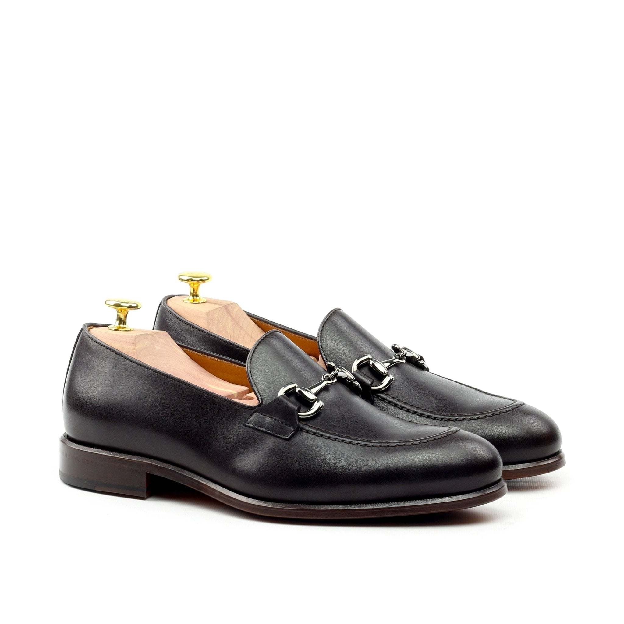 A pair of black leather slip-on horse bit loafers on a white background, showcasing the front view with the interior lining and the metallic horse bit detail.