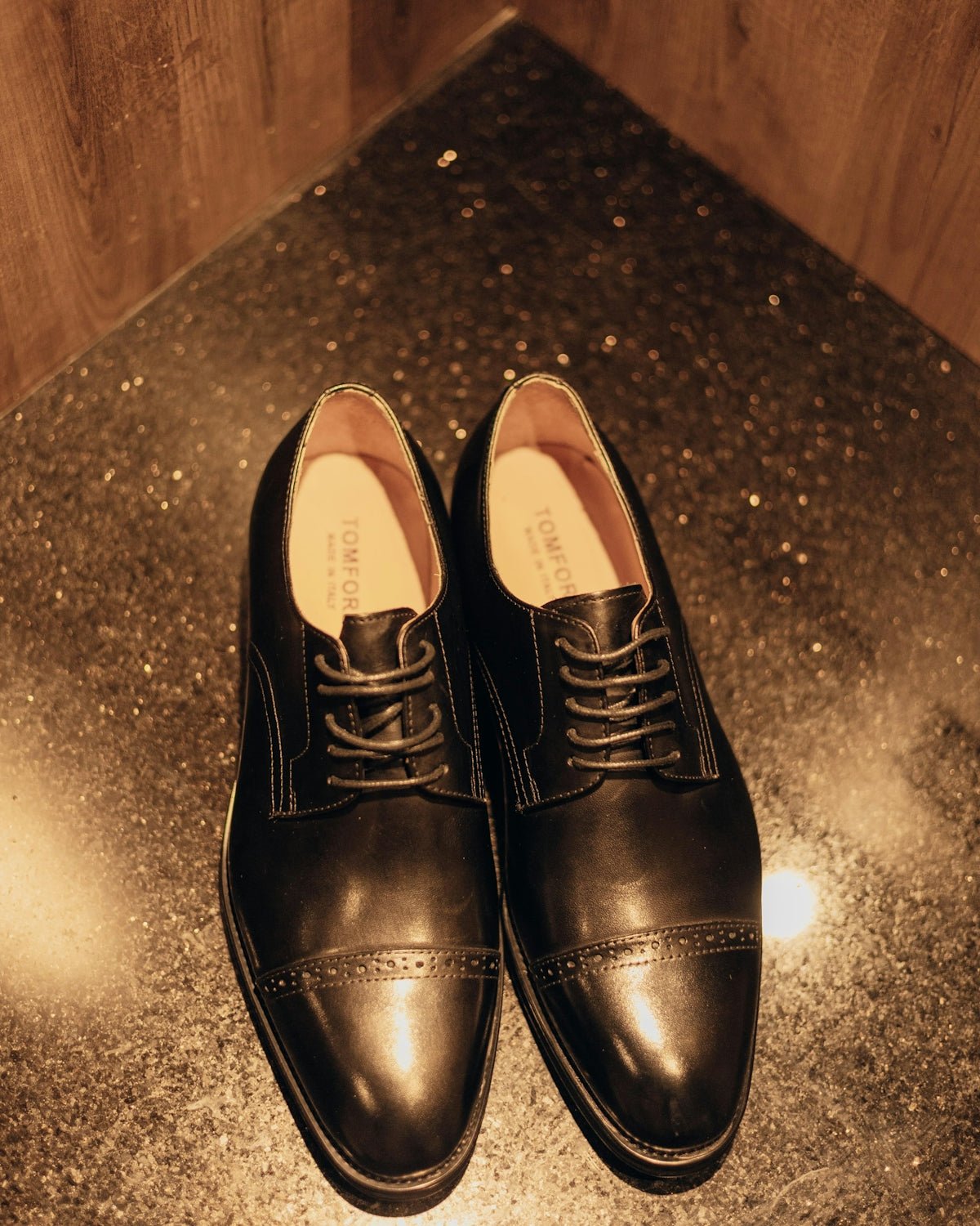 Formal dark leather shoes on a speckled floor.