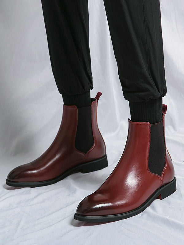 Red leather Chelsea boots with black soles worn by a person on a white background