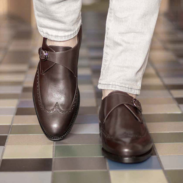 Brown leather shoes worn with light-colored pants on a tiled floor.