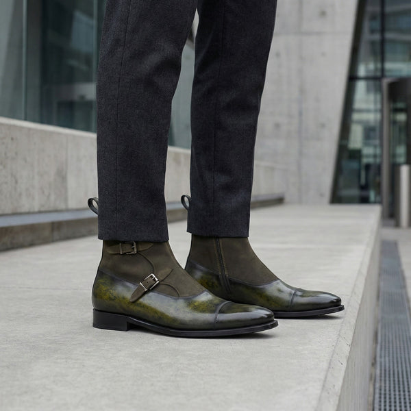 Person wearing dark green leather shoes with a building in the background
