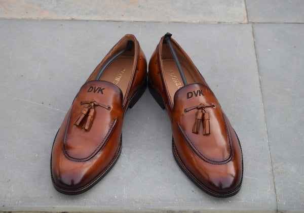 A pair of brown handmade tassel leather loafers with a label indicating 'Your Name Initials' on the top side.