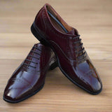 A pair of oxblood red leather Oxford dress shoes with a brogue design, laced up, on a wooden floor.