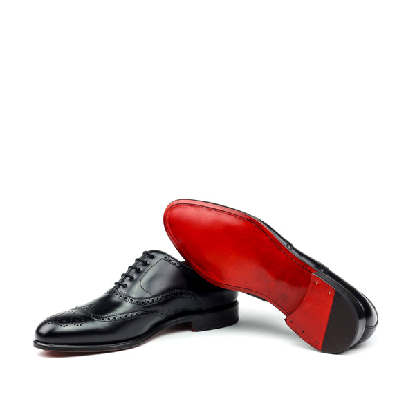 A pair of black brogue Oxford dress shoes with red bottom sole and traditional wingtip design.